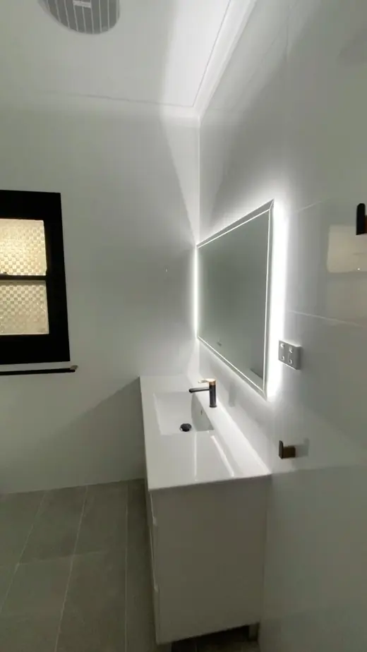 Renovated bathroom with a backlit mirror and white vanity