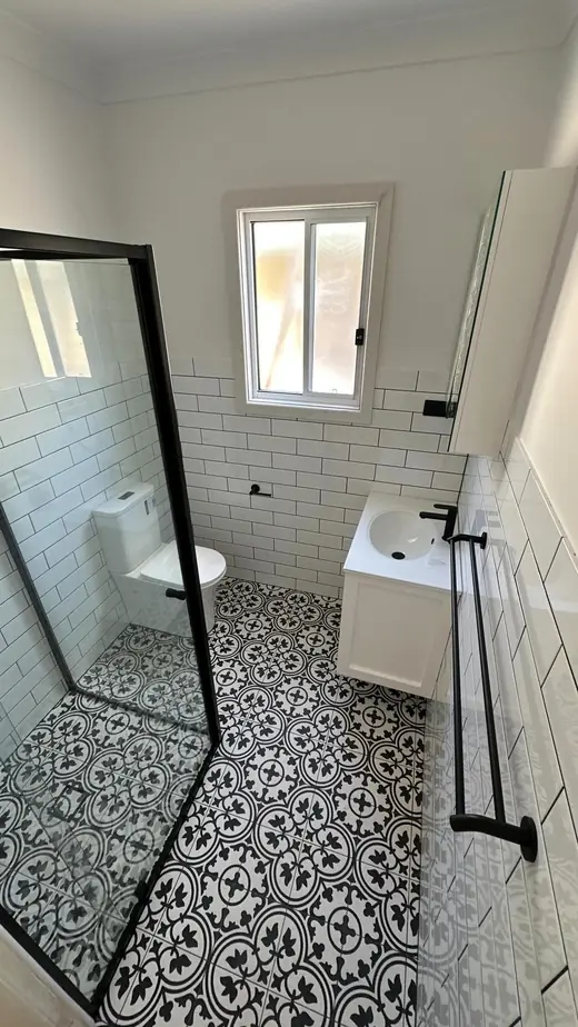 Renovated bathroom with patterned floor tiles and a black shower frame